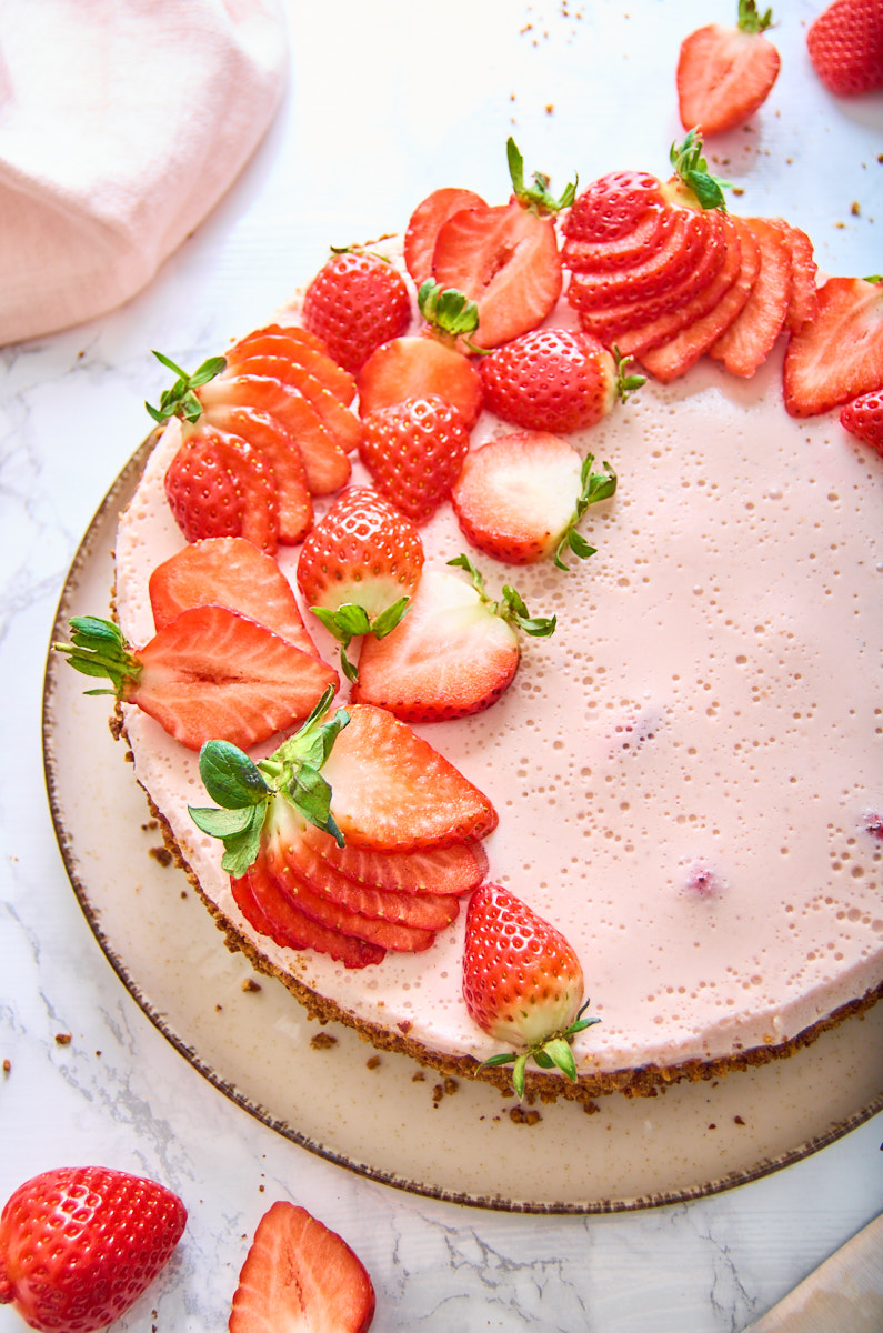 Strawberry Protein Mousse Pie on a plate, decorated with strawberries. Some half, some fanned out, some with their greens attached. From the top down.
