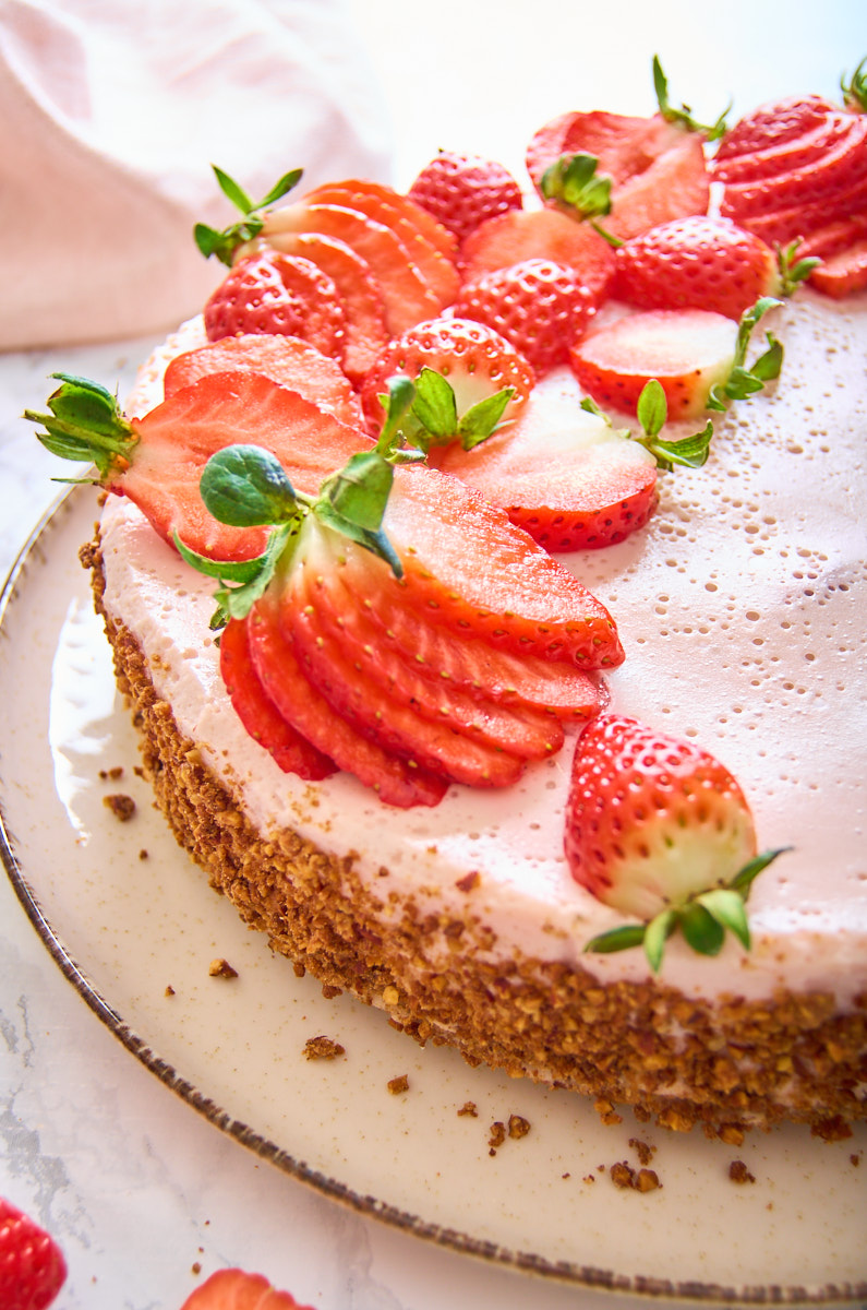 Strawberry Protein Mousse Pie on a plate, decorated with strawberries. Some half, some fanned out, some with their greens attached. Photo from the font, showing the left half of the pie.