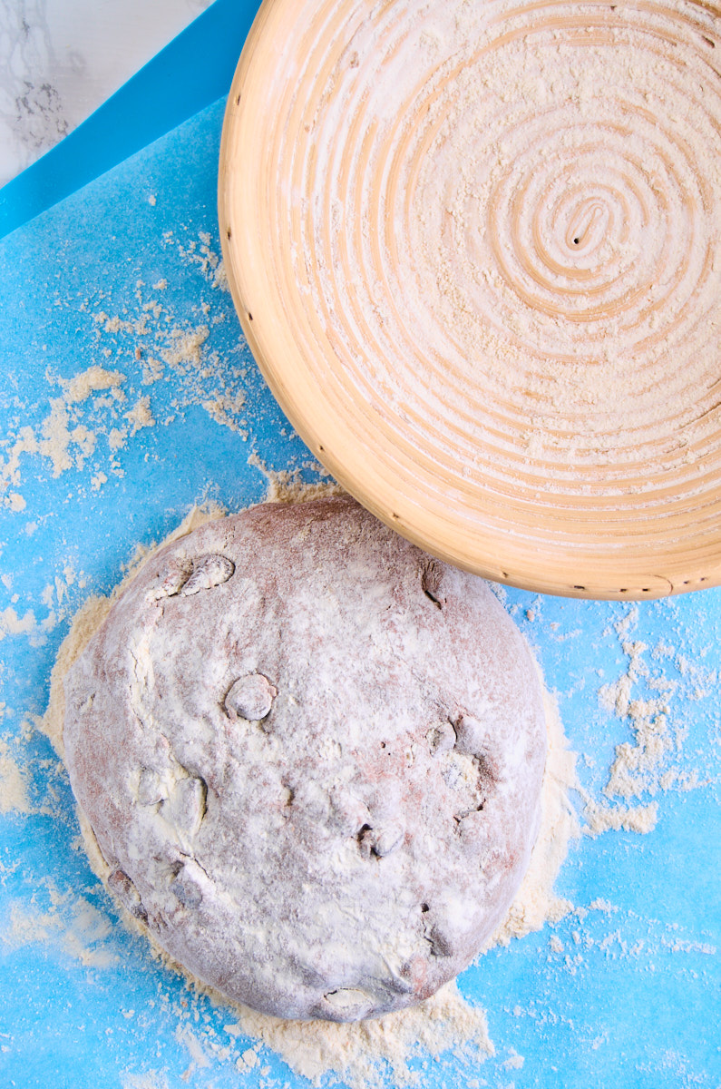 Black Garlic Sourdough Bread with Chocolate dough heavily floured on a silicone mat beside a banneton.