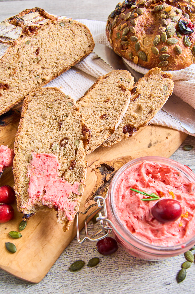 Cranberry Buckwheat Sourdough Bread with Rosemary and Pumpkin Seeds_ baked, 3 slices lying n front, showing the cranberry studded bread. Whipped cranberry butter beside the bread, some of it spread on a slice.
