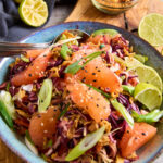Asian Slaw with Grapefruit in a blue bowl, topped with sliced spring onions and sesame seeds